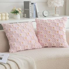 two pink pillows sitting on top of a couch next to a white book shelf with books