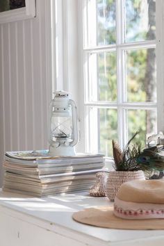 a stack of books sitting on top of a white table next to a hat and window