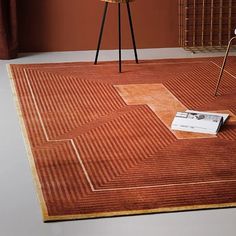 an orange rug is on the floor in front of a chair and table with a magazine