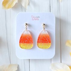 orange and yellow earrings with tiny glitters on them sitting on a white card next to flowers