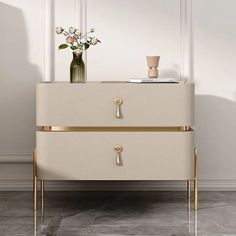 a white dresser with gold handles and flowers in a vase next to it on a marble floor