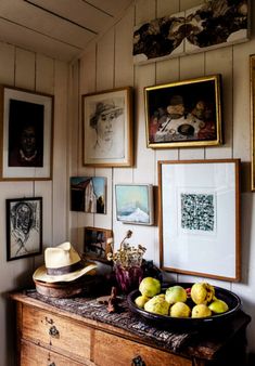 a bowl of fruit on top of a wooden dresser in a room with many framed pictures