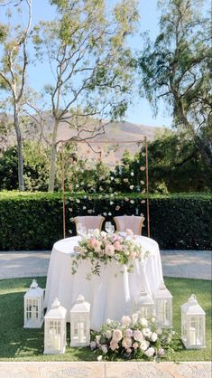 an outdoor table with lanterns and flowers on the grass at a wedding in front of a hedge