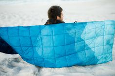 a young boy sitting in the sand with a blue blanket over his face and back