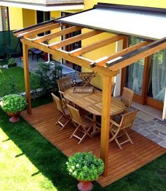 an outdoor dining area with table and chairs on the grass next to a yellow building