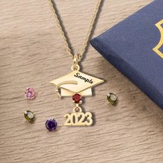 a gold graduation necklace with the number twenty two and three different colored stones on it