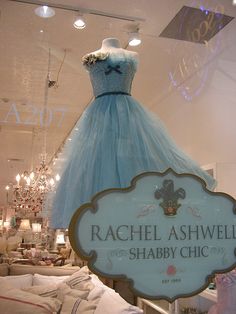 a blue dress is on display in a store window with chandelier and pillows