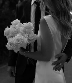 the bride and groom are walking down the street holding bouquets of white roses in their hands