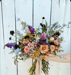 a woman holding a bouquet of flowers in front of a white wooden fence with blue trim