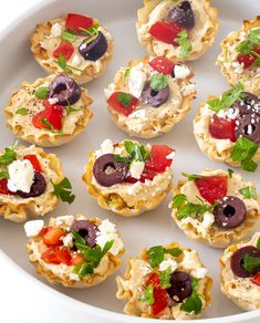 small appetizers with olives, tomatoes and feta cheese are arranged on a white platter