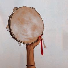 a person holding up a drum in front of a white wall with a red ribbon