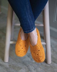 a woman sitting on top of a wooden chair wearing orange slippers with holes in them