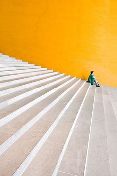 a person sitting on the steps in front of a yellow wall with white stairs next to it