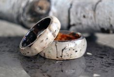 two wedding rings sitting next to each other on top of a metal table with wood logs in the background