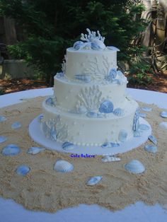 a three tiered wedding cake sitting on top of a table covered in sand and sea shells