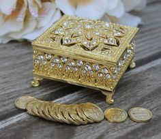 a gold jewelry box sitting on top of a wooden table next to some coins and flowers