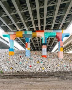 an underpass with colorful sculptures on the ground and rocks underneath it in front of a bridge