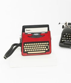 an old fashioned red typewriter sitting next to another typewriter on a white surface