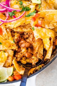 a skillet filled with mexican food and garnished with cilantro, red onion, green onions