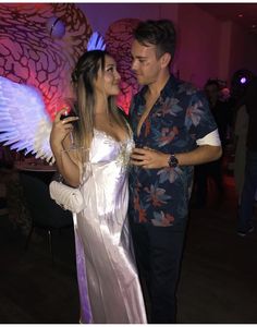 a man and woman standing next to each other in front of a wall with angel wings