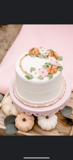 a white cake sitting on top of a wooden table next to flowers and pumpkins