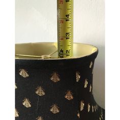 a black and gold lamp shade with bees on it next to a tape measure ruler