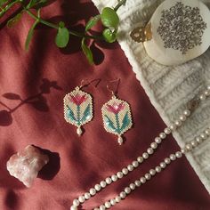 a pair of beaded earrings sitting on top of a red cloth next to pearls