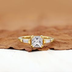 a gold and white ring with a princess cut diamond in the center on top of a leaf