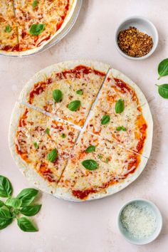 a pizza cut into eight slices on top of a white plate next to basil leaves