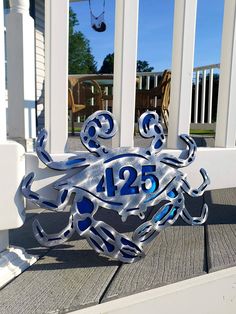 a metal crab sitting on top of a wooden deck next to a white fence and blue railing