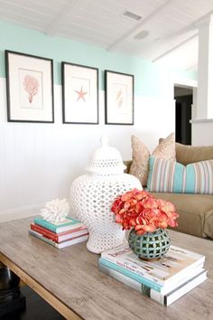 a coffee table with books and flowers on it in front of a couch, two pictures hanging on the wall