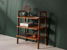 a wooden shelf with books on it next to a green wall and potted plant