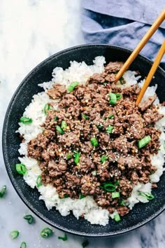 a black bowl filled with rice and ground beef next to chopsticks in it