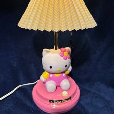 a hello kitty lamp sitting on top of a pink base with a yellow and white shade