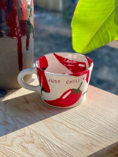 two red and white cups sitting on top of a wooden table next to a green leaf