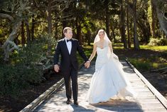 a bride and groom walking on a wooden bridge