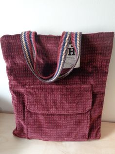 Handmade, one-of-a-kind tote or book bag by H Bags. Perfect if your school colors are dark red and navy blue.  Created by H bags from recycled fabrics and supplies.  Exterior is a heavy brushed corduroy type fabric in dark red. There is a large pocket (9.5" x 8.5") on the front with a flap covering the opening of the pocket. Perfect for snacks or other non-valuables. The inside of the bag is dark grey vinyl. Unfinished edges are covered with navy blue cotton trim. Note there is a blue leather key holder with dark brass hardware attached to the inside of the bag. Handles are striped cotton strapping in maroon, mauve, navy, cream and brown. Dimensions: 15" wide by 16.5" tall.  Spot clean. Note: Bag will be folded in half for shipment and shipped USPS Ground for economy unless buyer prefers P Handmade Burgundy Bag For Daily Use, Handmade Burgundy Shoulder Bag For Daily Use, Handmade Burgundy Shoulder Bag For Everyday, Burgundy Shoulder Bag For School, Burgundy School Shoulder Bag, Handmade Red School Bag, Handmade Burgundy Rectangular Bag, Handmade Red Backpack, Leather Key Holder