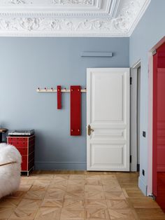 a room with blue walls and white trim, red accents on the door, and a fur covered bench