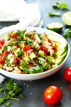 a salad in a bowl with tomatoes, avocado and chicken on the side