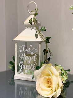 a small white lantern sitting on top of a glass table next to a yellow rose