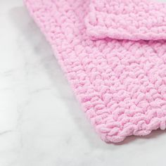 a pink crocheted blanket laying on top of a white countertop next to a toothbrush