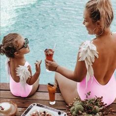 two women in pink swimsuits sitting at a table with food and drinks on it