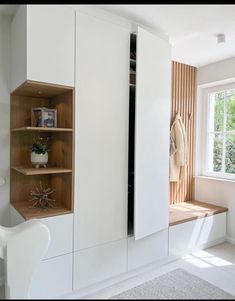 a white cabinet with shelves and drawers in a room next to a window, near a chair