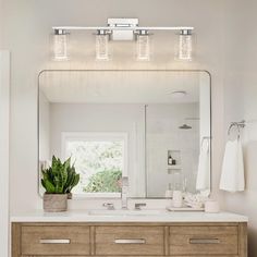 a bathroom vanity with three lights and a mirror above it, along with a potted plant