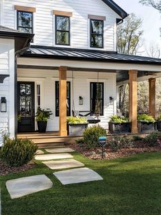 a white house with black trim and wooden pillars on the front porch, surrounded by green grass