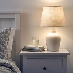 a white lamp sitting on top of a night stand next to a nightstand with books