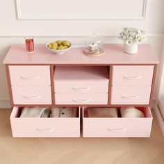 a pink dresser with drawers and baskets on top, filled with items such as lemons