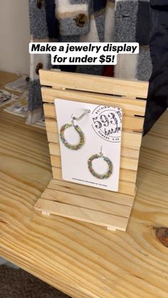 a pair of earrings sitting on top of a wooden table next to a sign that says make a jewelry display for under $ 6