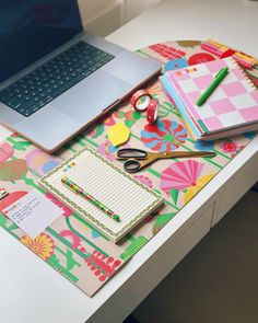 an open laptop computer sitting on top of a desk next to a notebook and pen