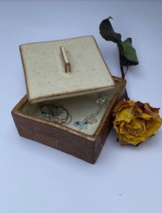 an open box with jewelry and a flower on the side, sitting next to it